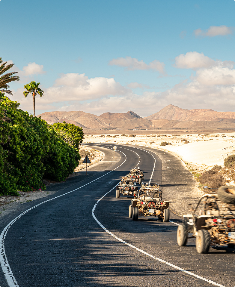 Desert buggy convoy on winding road, desert landscape.