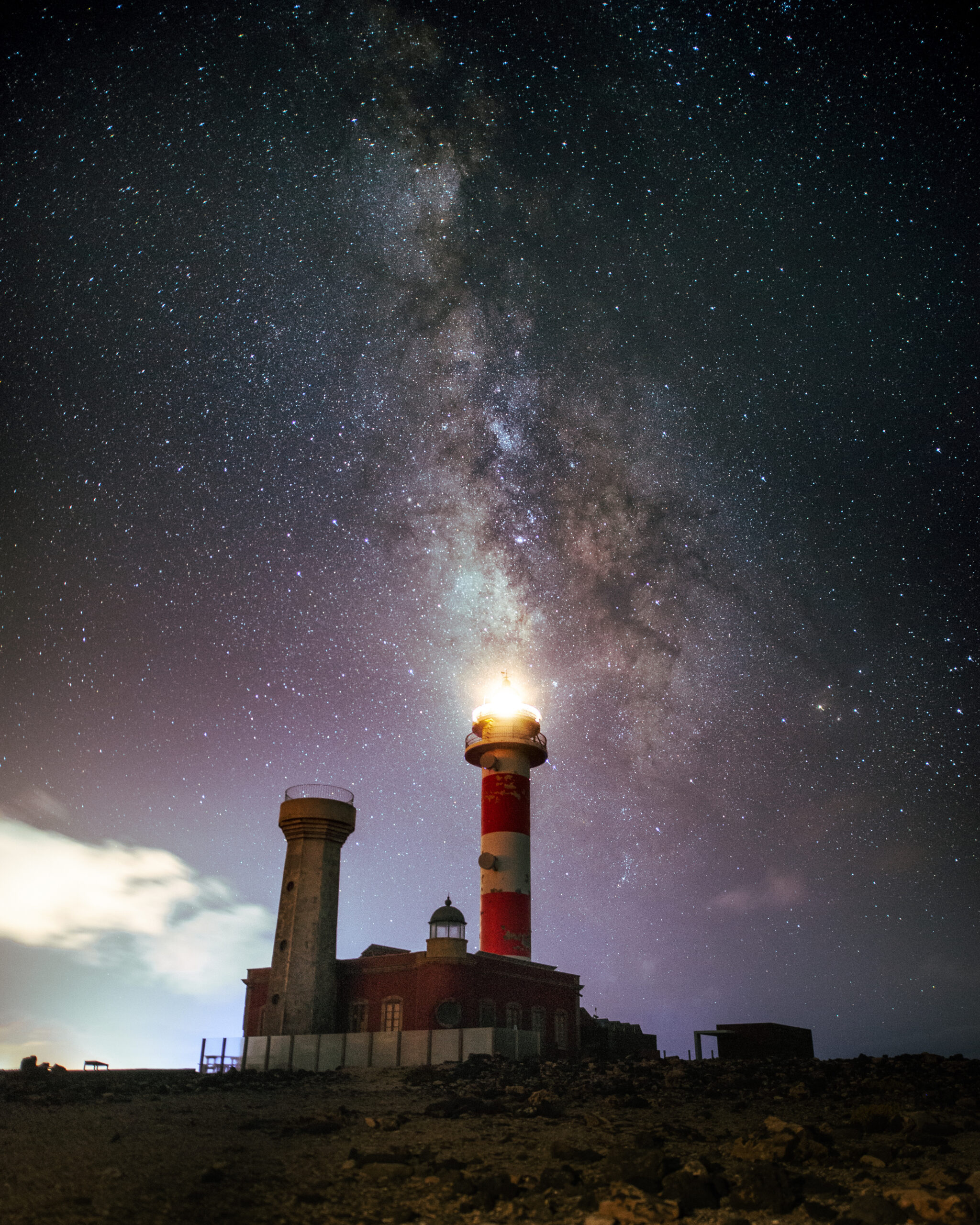 Lighthouse illuminated against a vibrant Milky Way nightscape.