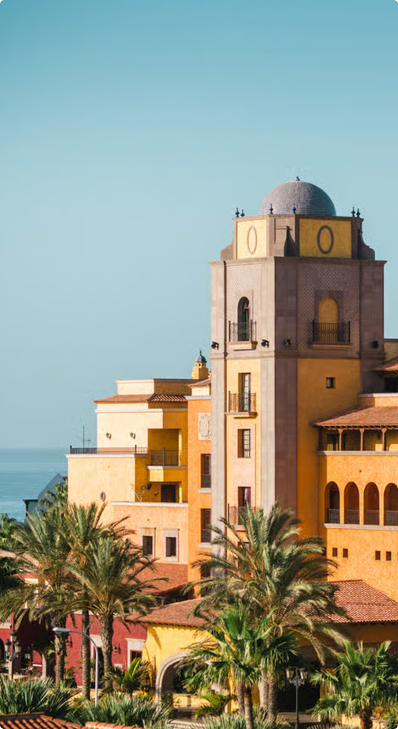 Coastal Mediterranean architecture; sun-drenched buildings, palm trees.
