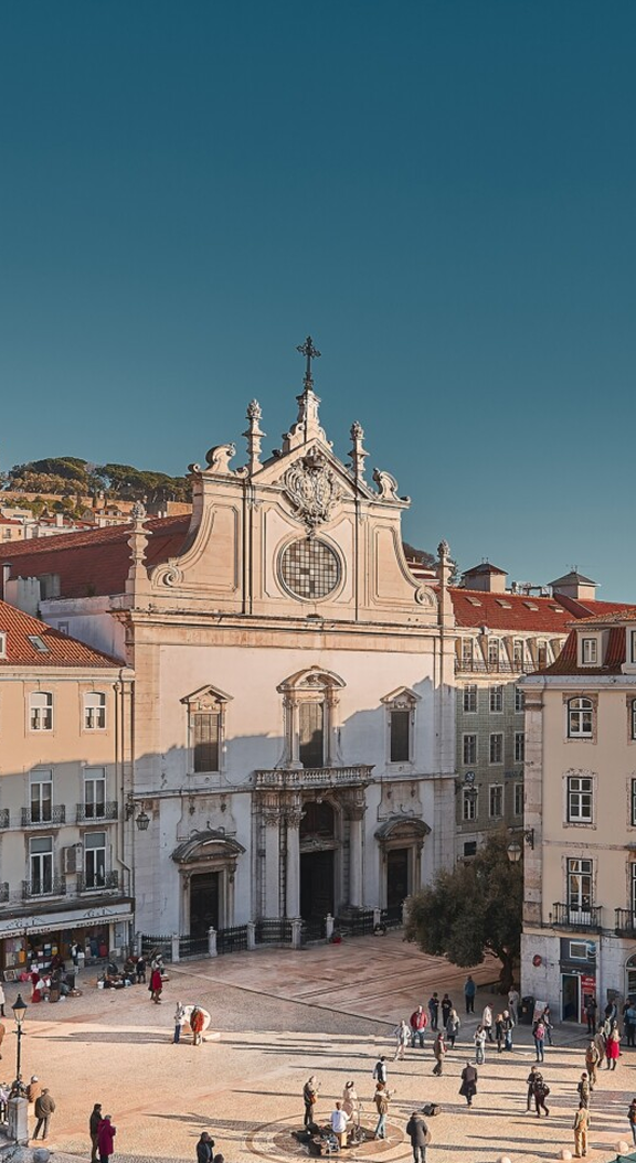 Sunlit Lisbon church facade, square with people.