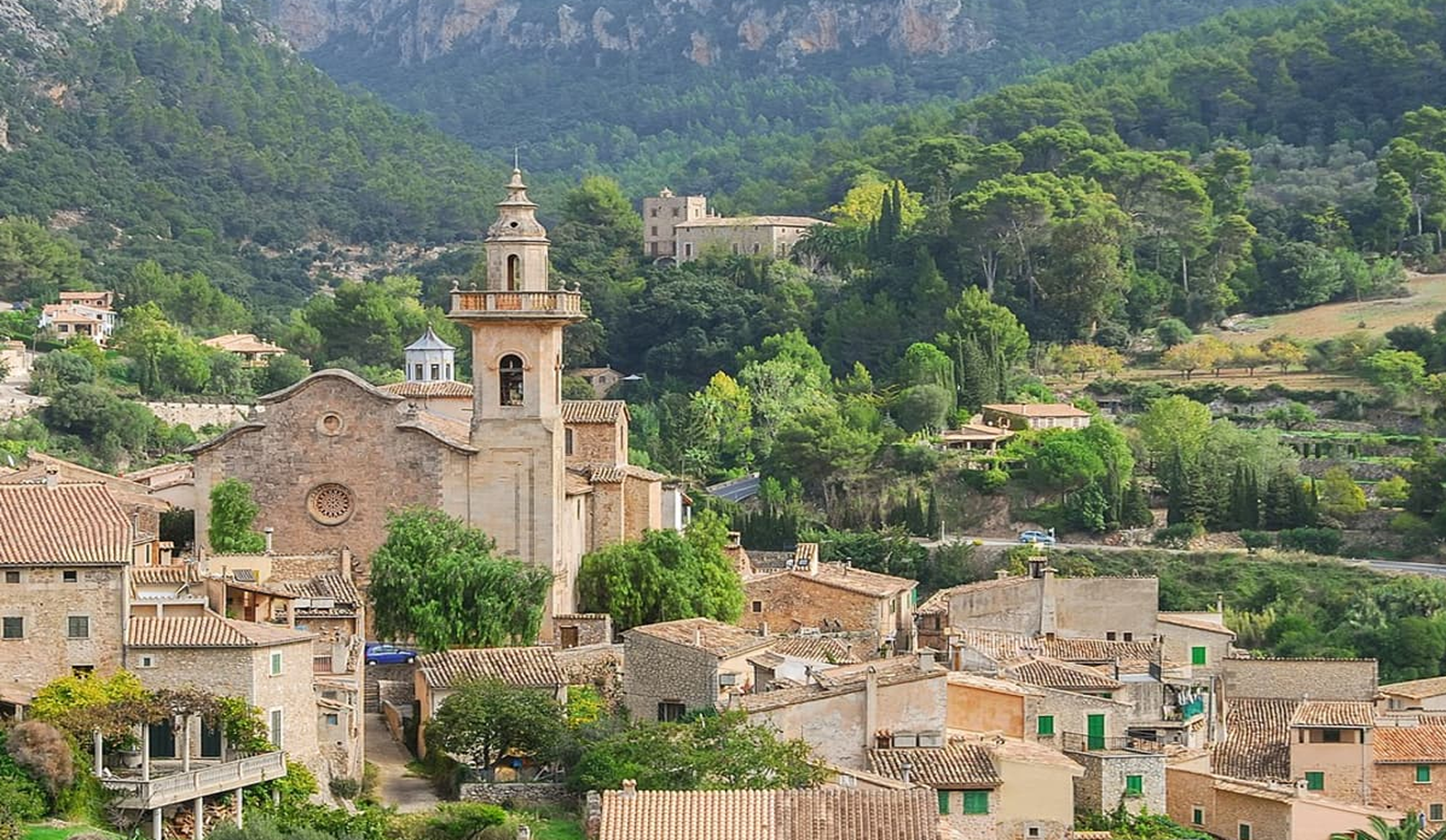 Valldemossa village, hilltop church & stone houses nestled in green mountains.