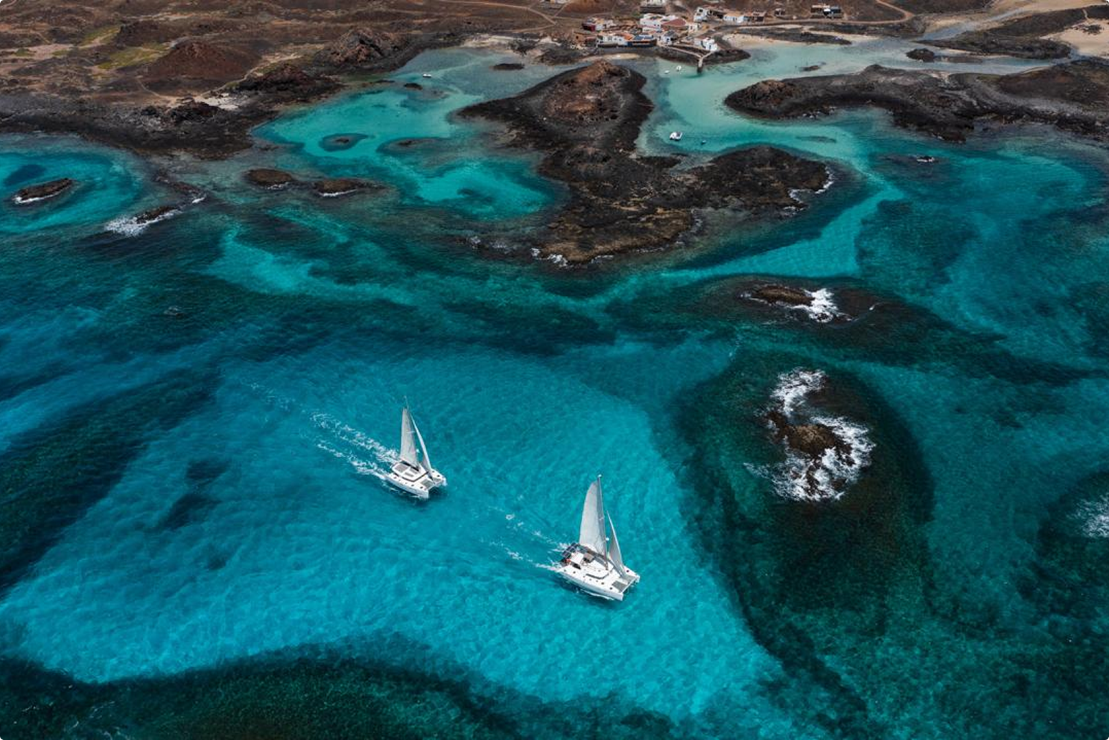Lobos Island catamaran voyage: Two catamarans sail turquoise waters near volcanic coast.