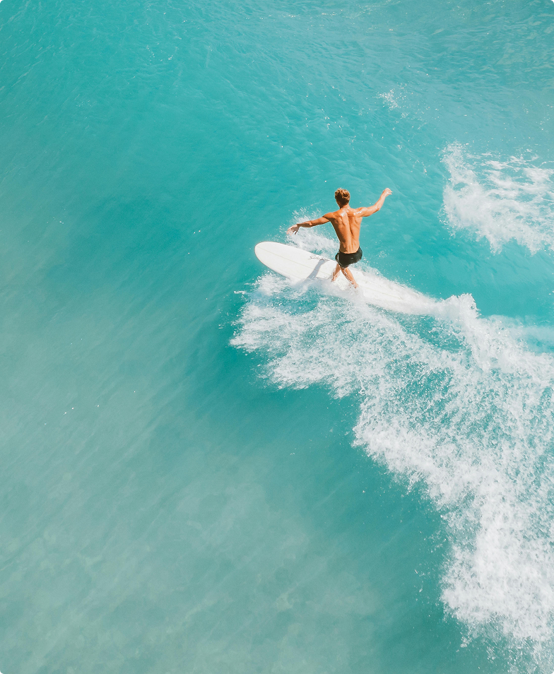 Surfer riding turquoise wave, aerial view.