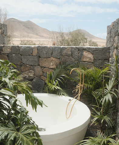 Outdoor tub with gold faucet, nestled in volcanic landscape.