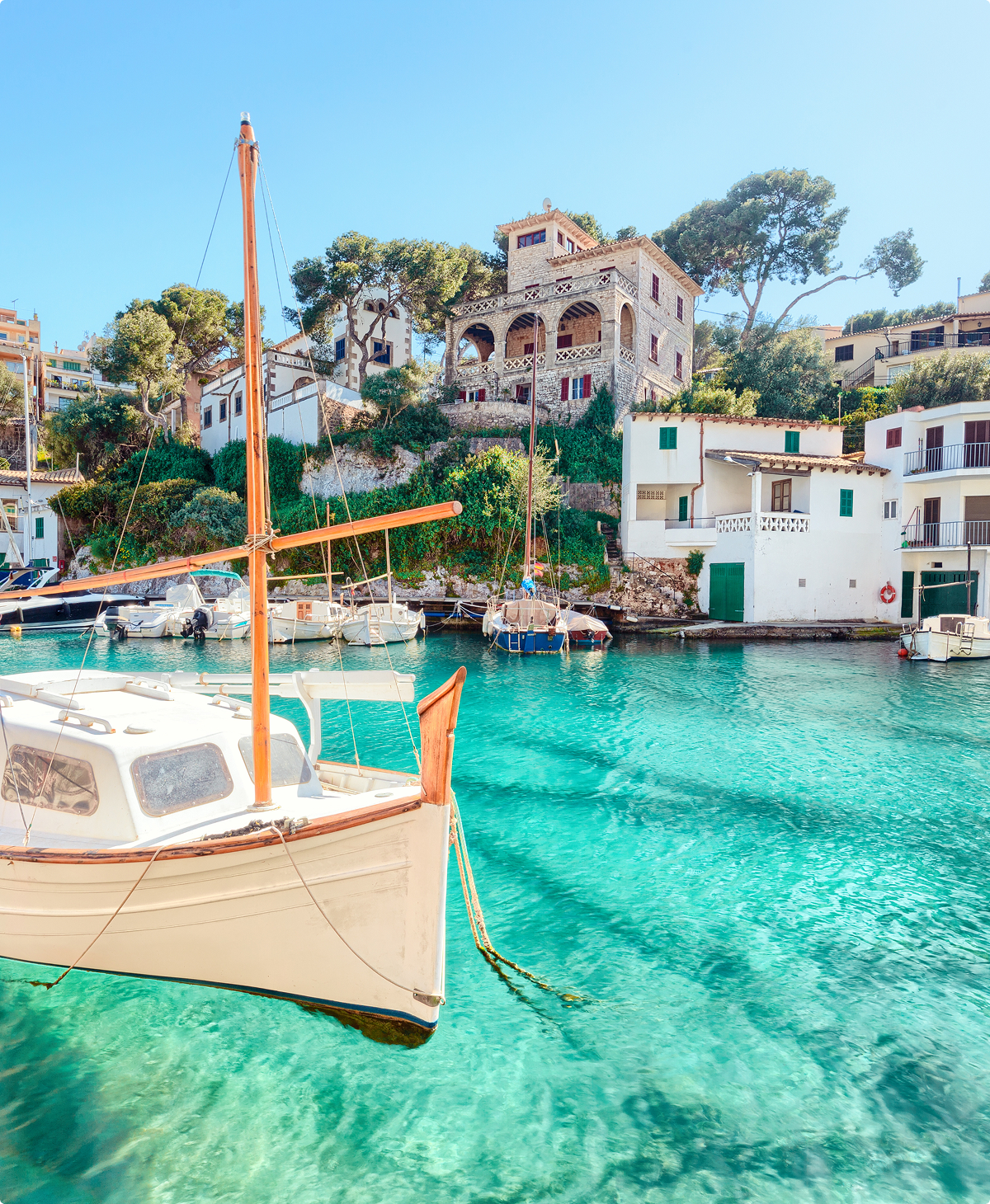 Menorca: Turquoise waters, coastal homes, and a sailboat in a picturesque harbor.