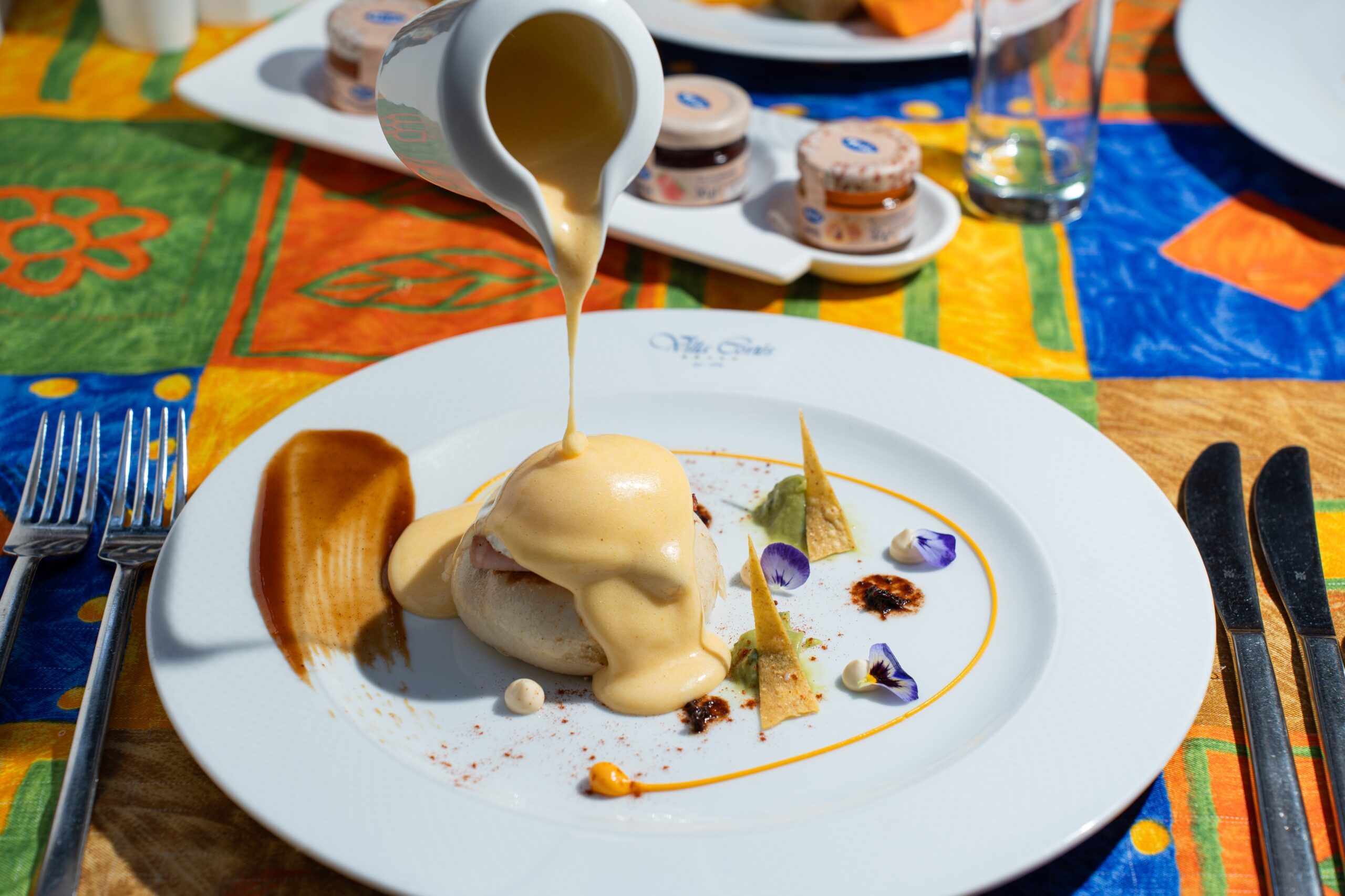 Gourmet Eggs Benedict with hollandaise sauce, garnished with edible flowers and tortilla chips.