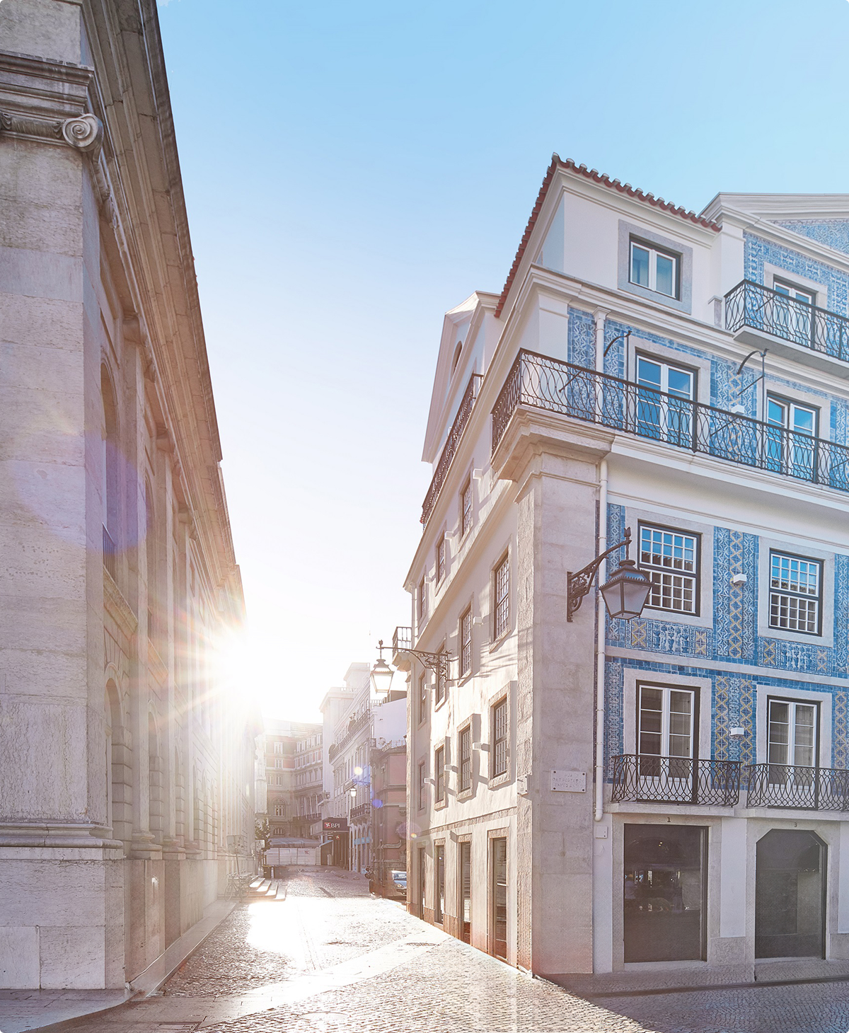 Lisbon street scene: AURA Partners location. Sunlit cobblestone street with historic buildings.